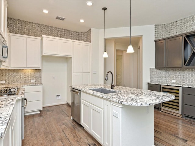 kitchen with visible vents, a center island with sink, a sink, wine cooler, and stainless steel appliances