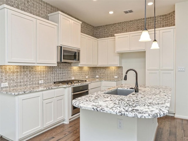 kitchen with light stone countertops, appliances with stainless steel finishes, a sink, and dark wood finished floors