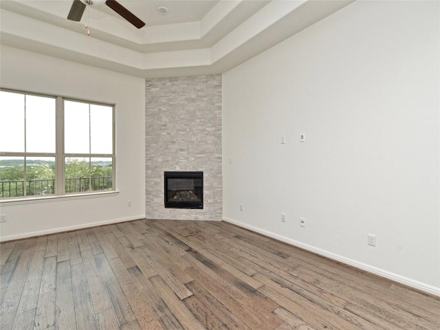 unfurnished living room with a fireplace, a ceiling fan, baseboards, wood finished floors, and a tray ceiling