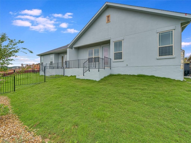 back of house with a lawn, fence, and stucco siding