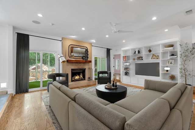 living area featuring visible vents, recessed lighting, a warm lit fireplace, and light wood-type flooring