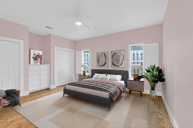 bedroom with a ceiling fan, visible vents, wood finished floors, baseboards, and multiple closets