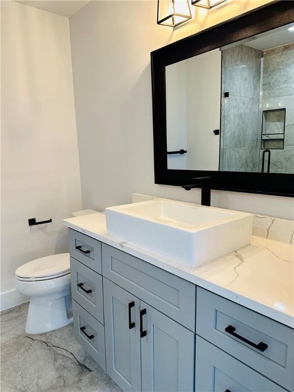 full bathroom featuring vanity, marble finish floor, toilet, baseboards, and a stall shower