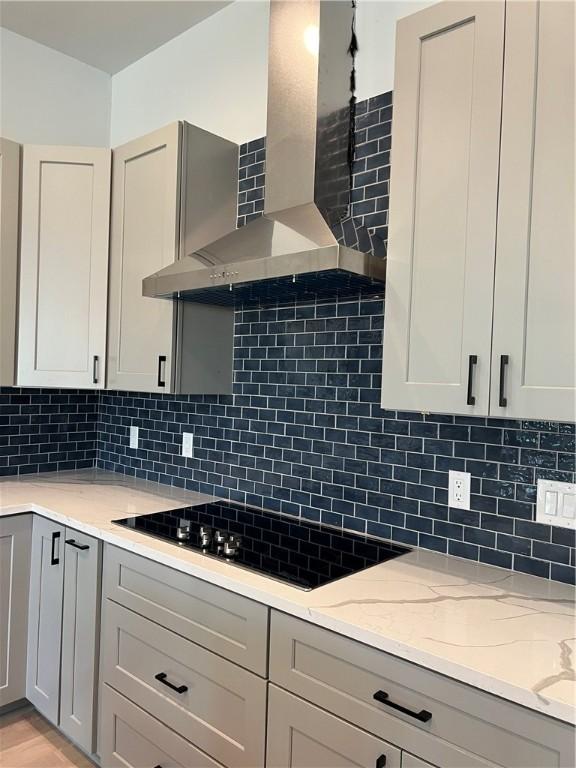 kitchen with gray cabinets, light stone countertops, wall chimney exhaust hood, and black electric cooktop
