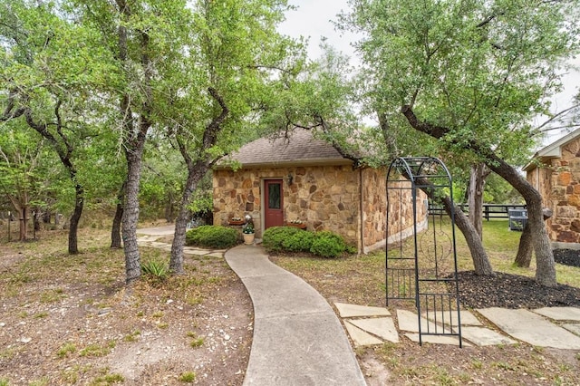 bungalow-style house with fence, a shingled roof, and stone siding