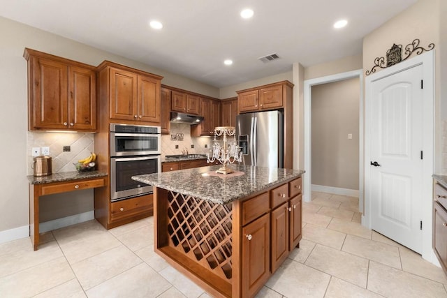 kitchen featuring brown cabinets, dark stone countertops, stainless steel appliances, backsplash, and visible vents