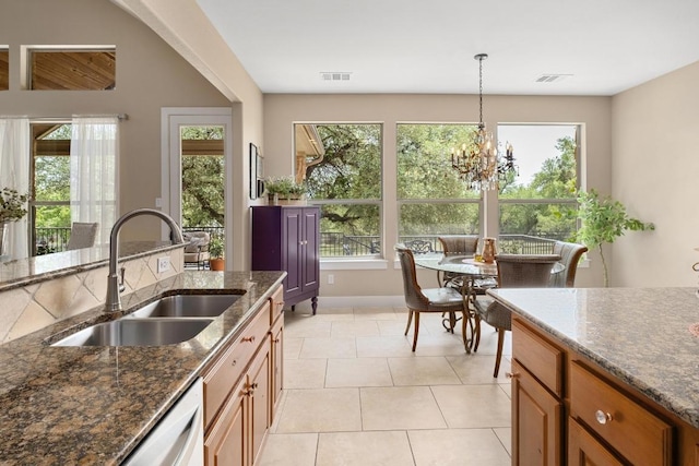 kitchen with brown cabinetry, visible vents, a sink, baseboards, and dark stone countertops