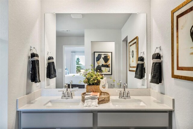 full bath featuring double vanity, a textured wall, and a sink