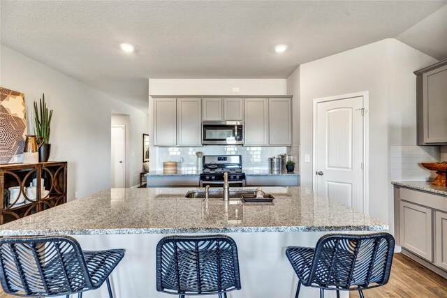 kitchen with decorative backsplash, gray cabinets, a breakfast bar area, light stone counters, and stainless steel appliances