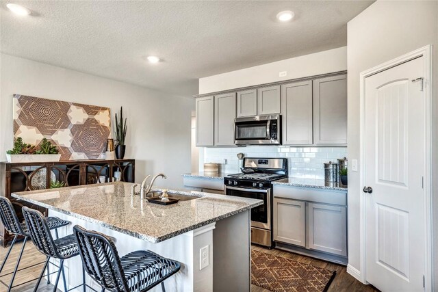kitchen with light stone counters, a sink, a kitchen breakfast bar, gray cabinets, and stainless steel appliances