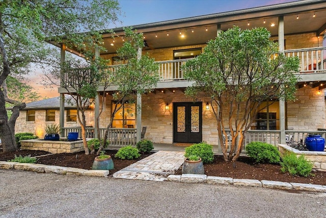 view of front of home featuring a porch, french doors, a balcony, and stone siding