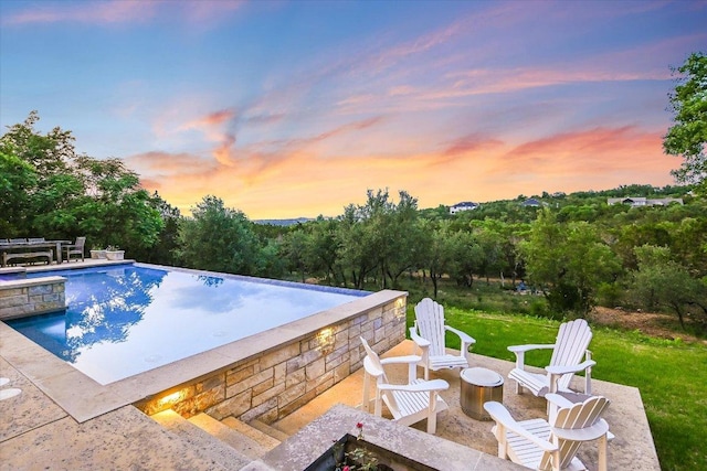 pool at dusk featuring a patio and an infinity pool