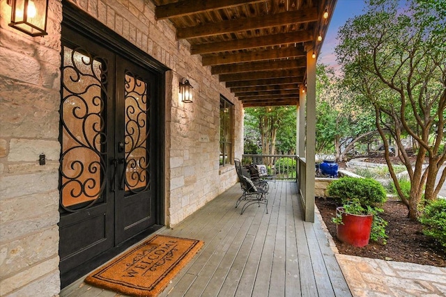 deck at dusk featuring covered porch and french doors