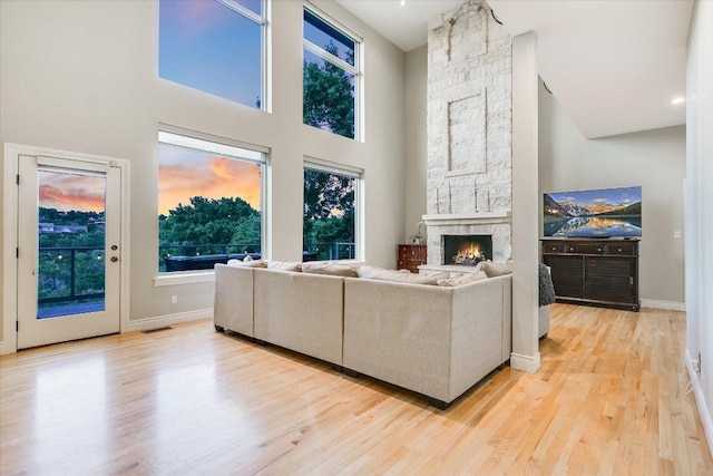 living room featuring a stone fireplace, visible vents, a towering ceiling, wood finished floors, and baseboards