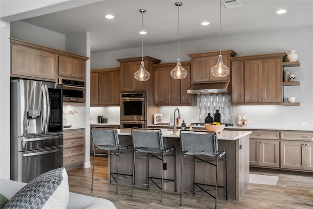 2033 Portobello Rd, Leander, TX 78641 - kitchen featuring stainless steel appliances, under cabinet range hood, light wood-style flooring, light countertops, and a kitchen bar
