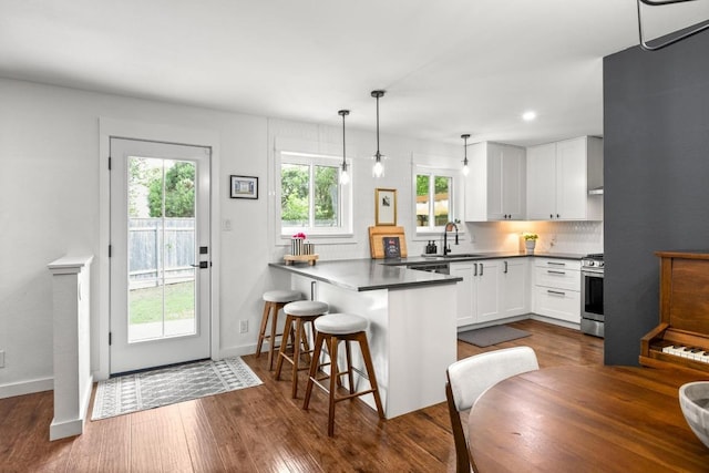 kitchen featuring dark wood-style flooring, stainless steel gas stove, a sink, white cabinets, and a peninsula