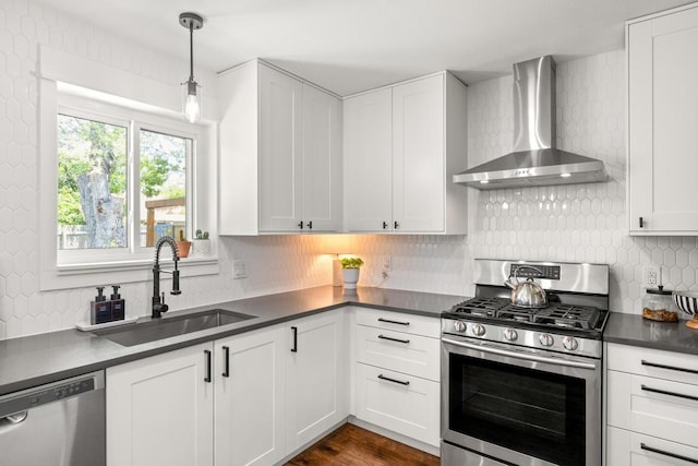 kitchen featuring wall chimney range hood, dark countertops, a sink, stainless steel appliances, and tasteful backsplash