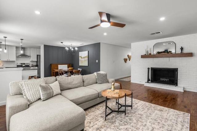 living room with light wood finished floors, a fireplace, ceiling fan with notable chandelier, baseboards, and visible vents