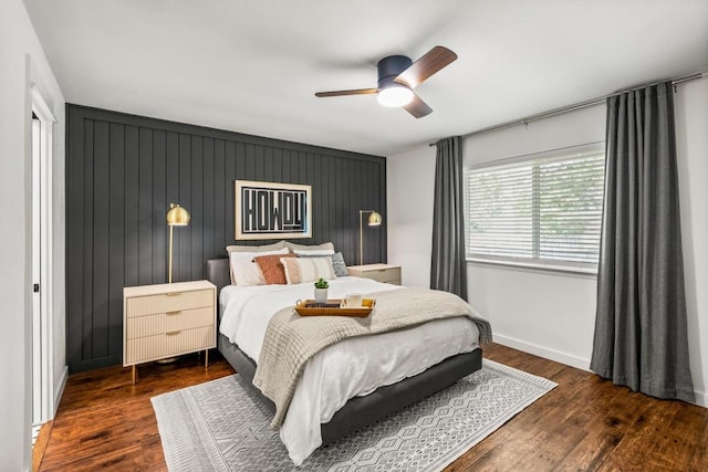bedroom with baseboards, an accent wall, a ceiling fan, and wood finished floors