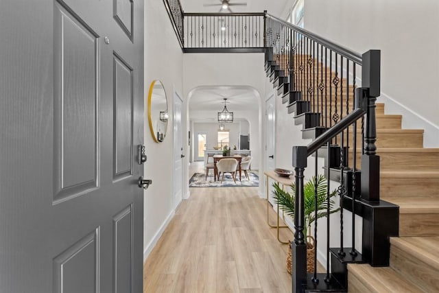 foyer featuring a towering ceiling, baseboards, ceiling fan, light wood-type flooring, and arched walkways
