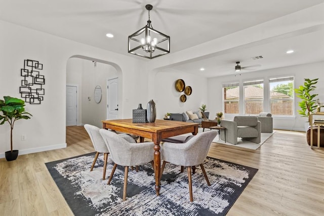 dining space with light wood-style floors, arched walkways, ceiling fan with notable chandelier, and recessed lighting