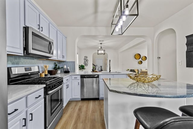 kitchen with light stone counters, arched walkways, stainless steel appliances, a peninsula, and light wood-type flooring