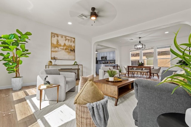 living area featuring light wood-style floors, ceiling fan with notable chandelier, recessed lighting, and visible vents