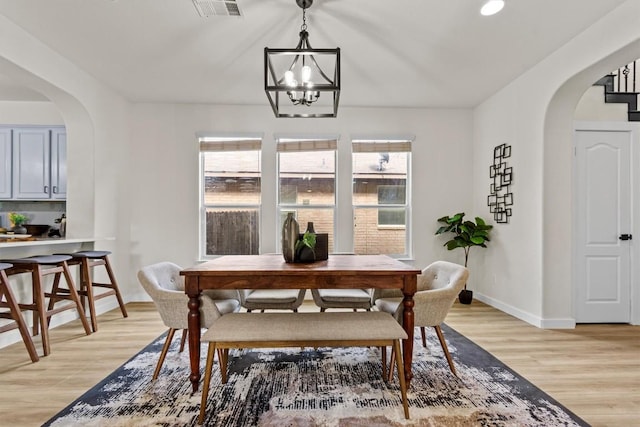 dining room with light wood-type flooring, arched walkways, a healthy amount of sunlight, and visible vents