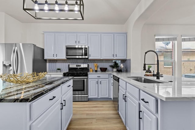 kitchen with stainless steel appliances, light stone counters, a sink, and tasteful backsplash
