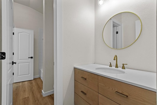 bathroom with a bathtub, walk in shower, wood finished floors, vanity, and baseboards