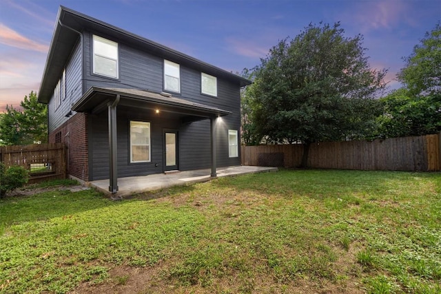 back of house at dusk with a fenced backyard, a lawn, and a patio area