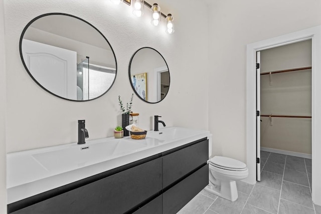 bathroom with double vanity, toilet, a sink, and a walk in closet