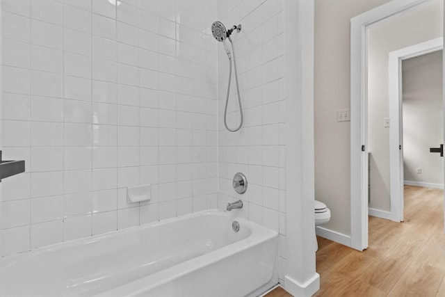 full bathroom with toilet, baseboards, washtub / shower combination, and wood finished floors