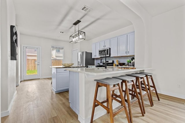 kitchen with visible vents, a peninsula, baseboards, light wood-style flooring, and stainless steel appliances