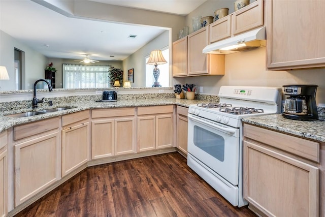 kitchen with white gas stove, a sink, dark wood-style floors, light brown cabinets, and under cabinet range hood