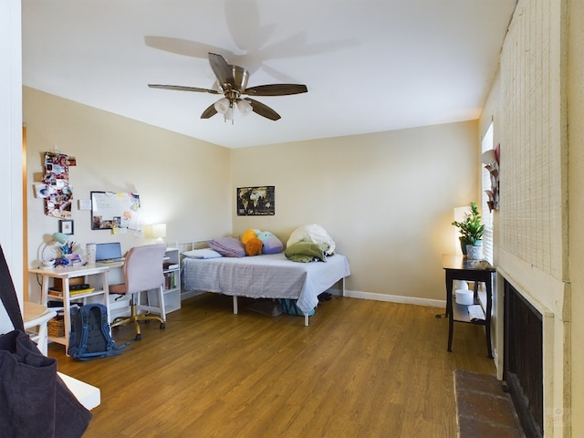 bedroom featuring baseboards, a fireplace with raised hearth, a ceiling fan, and wood finished floors