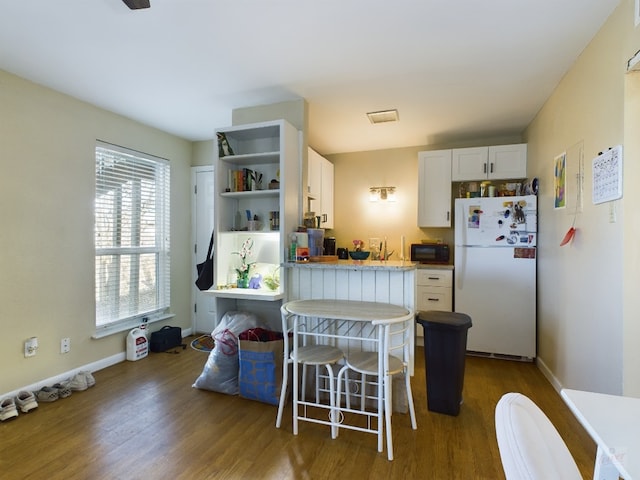 kitchen featuring open shelves, black microwave, freestanding refrigerator, white cabinetry, and wood finished floors