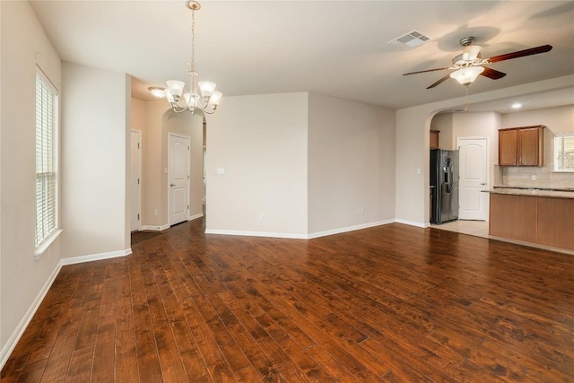 unfurnished living room featuring arched walkways, ceiling fan with notable chandelier, baseboards, visible vents, and dark wood-style floors