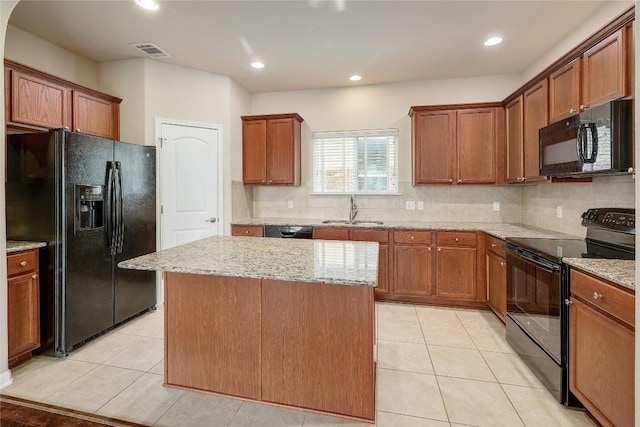 kitchen featuring light stone counters, a sink, black appliances, and tasteful backsplash