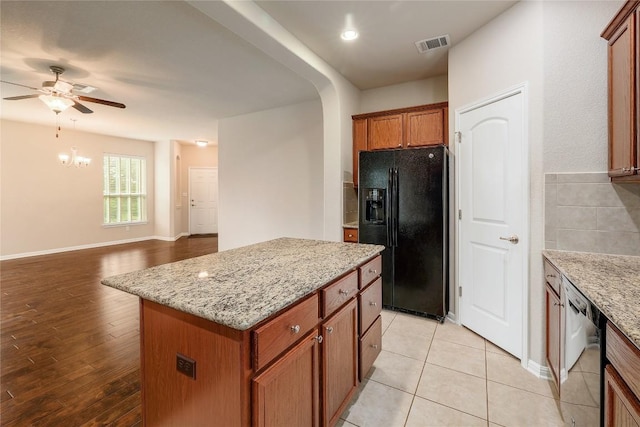 kitchen with visible vents, black refrigerator with ice dispenser, dishwashing machine, a center island, and ceiling fan with notable chandelier