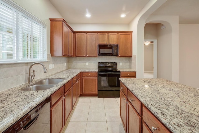 kitchen with a sink, backsplash, black appliances, and light stone countertops