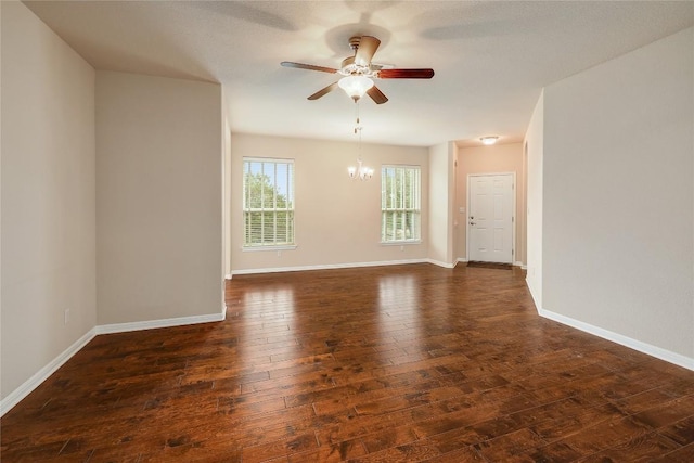 spare room with baseboards, ceiling fan with notable chandelier, and dark wood-style floors