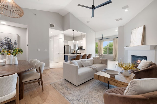 living room with vaulted ceiling, a ceiling fan, light wood finished floors, and visible vents
