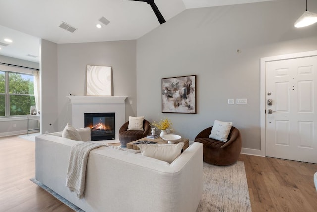 living room with a glass covered fireplace, baseboards, wood finished floors, lofted ceiling, and visible vents