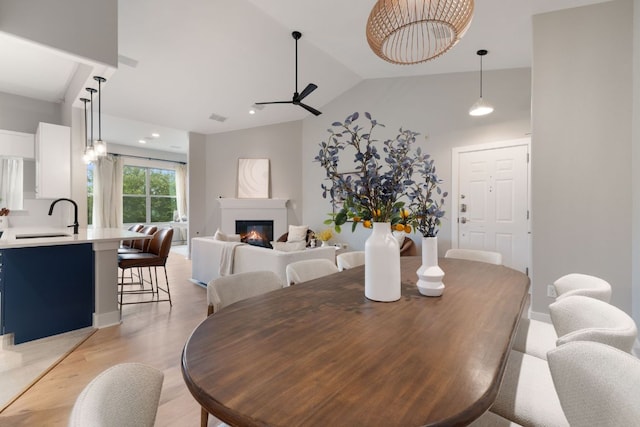 dining area featuring vaulted ceiling, a glass covered fireplace, ceiling fan with notable chandelier, and light wood-style floors