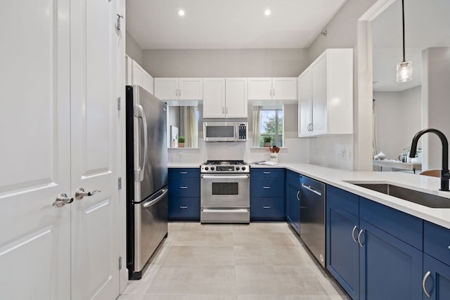 kitchen with appliances with stainless steel finishes, a sink, light countertops, blue cabinetry, and white cabinetry
