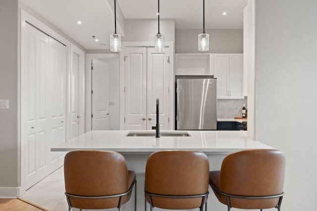 kitchen featuring white cabinets, a sink, light countertops, freestanding refrigerator, and decorative light fixtures