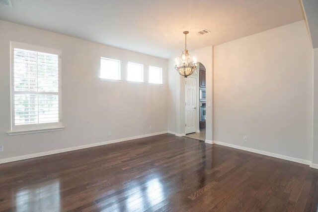 unfurnished room with baseboards, visible vents, wood finished floors, and a notable chandelier