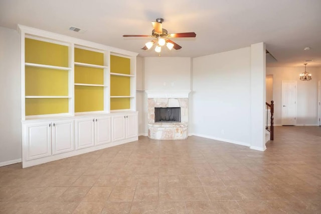 unfurnished living room featuring baseboards, ceiling fan with notable chandelier, a stone fireplace, and visible vents