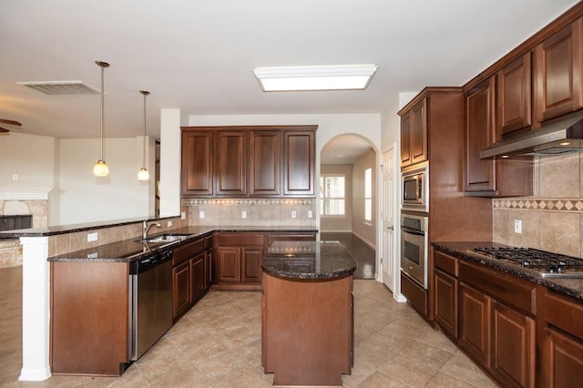 kitchen with appliances with stainless steel finishes, arched walkways, a sink, dark stone counters, and under cabinet range hood